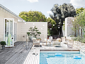 Neutral Exterior Backyard Wooden Deck with Pool and Plants and Brick Retainer Wall and Fairy Lights